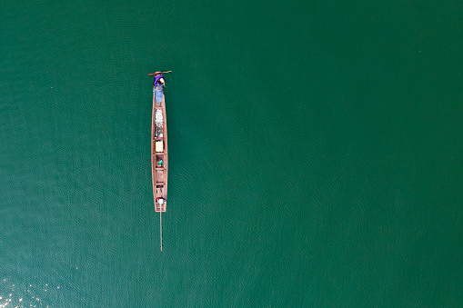 (View from above) Stunning aerial view of a traditional long-tail boat with a local person who is fishing in the waters of the Nam Ngum Reservoir, Thalat, northern Laos.