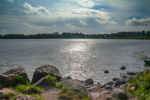 istock Dark sparkling lake with stones on shore is under a blue sky with clouds backlit by the sun at summer in Finland. 1130925349
