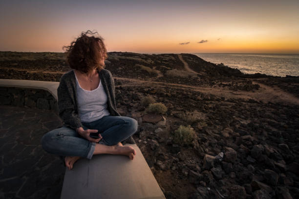 istock Woman Holding Mobile Phone While Sitting Outdoors At Sunset 1130930613