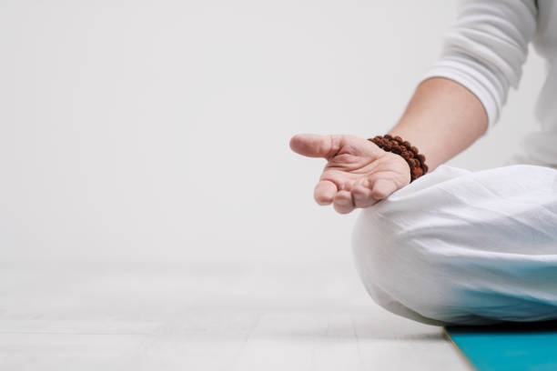 Concept of yoga and meditation. Close-up, hands of a man in white clothes, folded in prayer. White background and yellow-mini rubber mat. stock photo