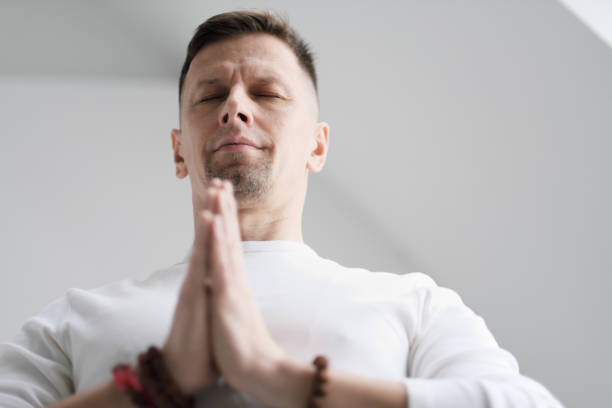 istock A man in white clothes on a white background with his hands folded on his chest. Meditation and prayer, yoga. 1130932036