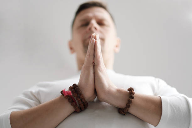 istock A man in white clothes on a white background with his hands folded on his chest. Meditation and prayer, yoga. 1130932090