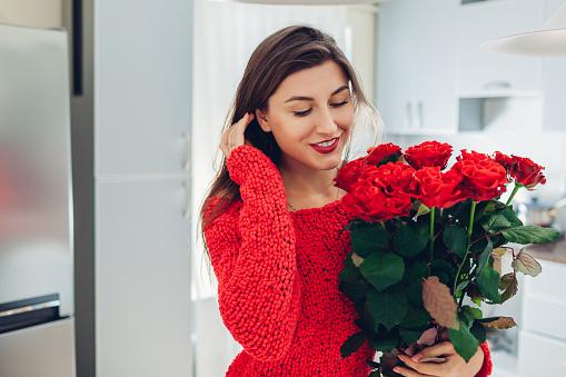 Young woman found red roses on kitchen. Happy girl smelling flowers. Women's day surprise