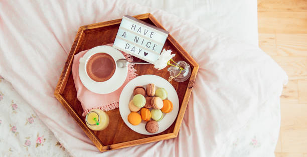 istock Top view Breakfast in bed with Have a nice day text on lighted box. Cup of coffee, juice, macaroons on wooden tray. Good morning mood. Hospitality, care, service concept. Wide banner. Copy space. 1130942912