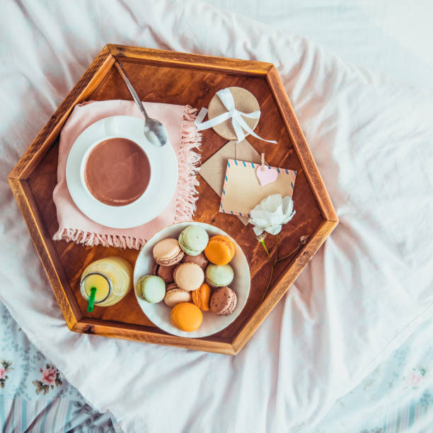 istock Breakfast in bed with empty blank card. Cup of coffee, juice, macaroons, flower and giftbox on wooden tray. Romantic breakfast in bed. Birthday, Valentine's day morning. Top view. Square. Copy space. 1130942915