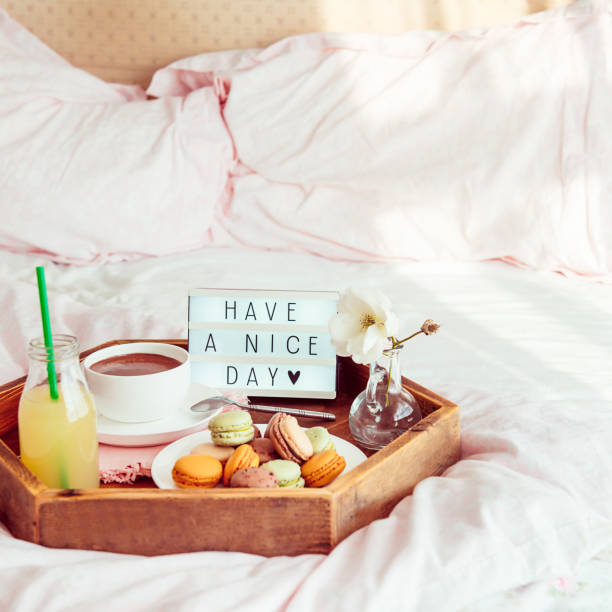 istock Breakfast in bed with Have a nice day text on lighted box. Cup of coffee, juice, macaroons, flower in vase on wooden tray. Good morning mood. Hospitality, care, service concept. Square. Copy space. 1130942960