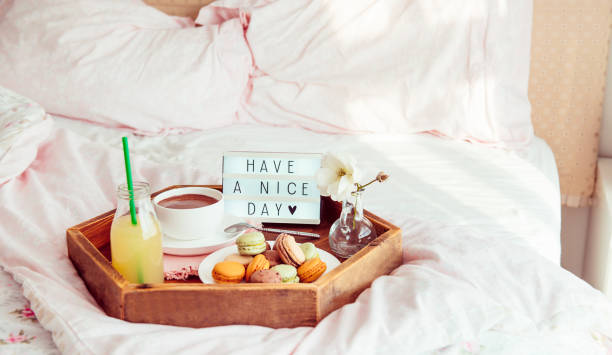 istock Breakfast in bed with Have a nice day text on lighted box. Coffee cup, juice, macaroons, flower in vase on wooden tray. Good morning mood. Hospitality, care, service concept. Wide banner. Copy space. 1130942963