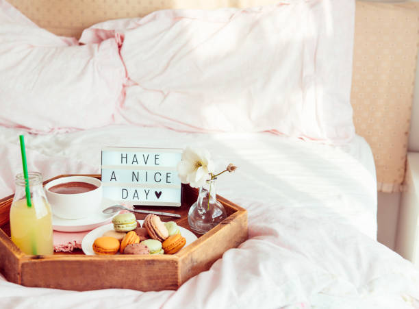 istock Breakfast in bed with Have a nice day text on lighted box. Cup of coffee, juice, macaroons, flower in vase on wooden tray. Good morning mood. Hospitality, care, service concept. Copy space. 1130942966