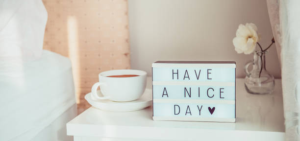 クローズアップライトボックス、コーヒーのカップと太陽光のベッドサイドテーブルに白い花に素敵な一日のテキストメッセージを持っています。おはようございます。ホスピタリティ、ケ� - wide awake ストックフォトと画像