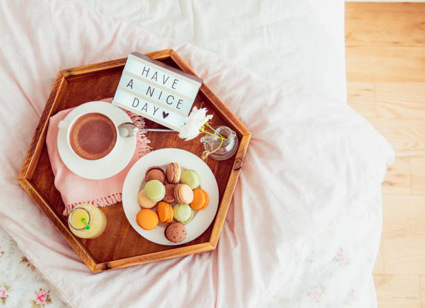istock Top view Breakfast in bed with Have a nice day text on lighted box. Cup of coffee, juice, macaroons, flower in vase on wooden tray. Good morning mood. Hospitality, care, service concept. Copy space. 1130942980