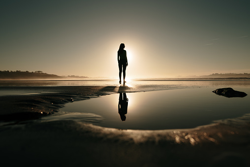 Young woman at a beach at sunset and her reflection on a puddle
