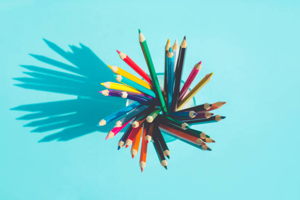 Top view of colorful pencil in glass with long shadow on pastel background
