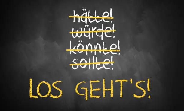 chalkboard with stroked words like could and should and "Let's go" in the middle in German