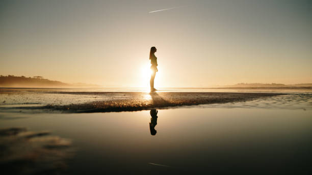 istock Young woman at beach at sunset and her reflection 1130951040