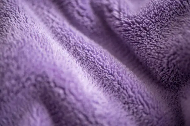 Purple delicate  background of nice furry cloth. Soft loose folds on the fabric of faux fur of lilac color as a textured background.