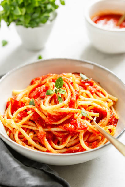 istock Traditional pasta with tomato and Greek basil sauce in a ceramic bowl on a white table. 1130951932