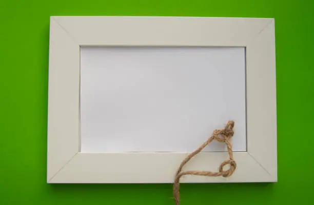 Photo of White blank frame with space for text lies on a green background, decorated with twine in knots, celebrating St. Patrick's Day