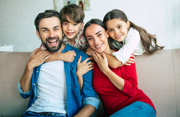 młoda szczęśliwa rodzina odpoczywa razem w domu uśmiechając się i przytulając - family sofa men sitting zdjęcia i obrazy z banku zdjęć