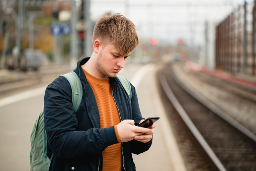 Young male adult using his smart phone while waiting for a train to arrive in Geneva.