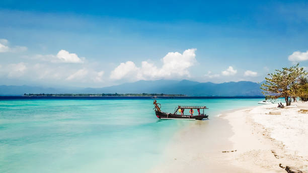 Gili Island - Boat to the Paradice A boat parked next to the shore on Gili Air, Lombok, Indonesia. Beautiful and clear water. In the back visible Mount Rinjani. Some trees on the shore, few clouds on the sky. bali stock pictures, royalty-free photos & images