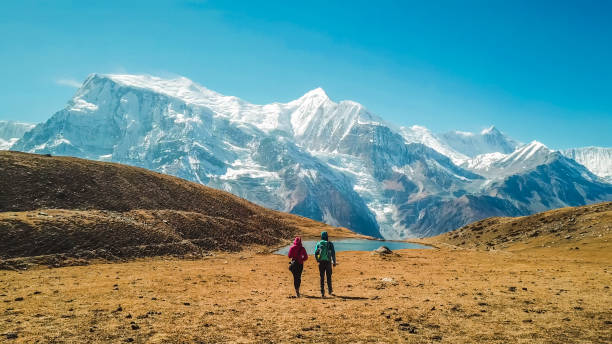 Nepal - Couple and the Ice lake with the view on Annapurna Chain A couple walking towards the Ice lake, as part of the Annapurna Circuit Trek, Himalayas, Nepal. Annapurna chain in the back, covered with snow. Clear weather, dry grass, snowy peaks. High altitude himalayas stock pictures, royalty-free photos & images
