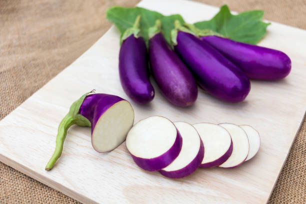 bakłażan fioletowy surowy na drewnianej desce do krojenia i na tle worka, jest pokarmem roślinnym dla zdrowia. - eggplant group of objects raw food eating zdjęcia i obrazy z banku zdjęć