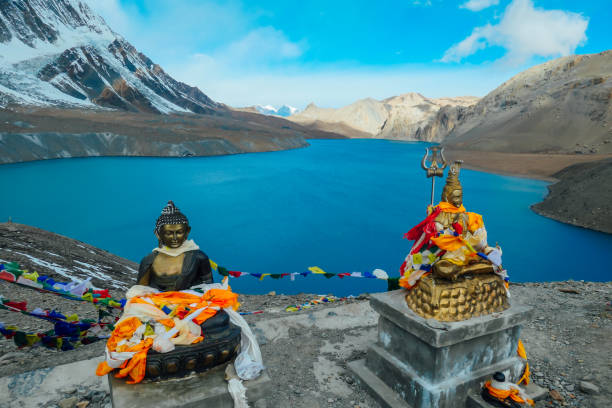 Nepal - Buddha statues at the Tilicho Lake Two Buddha statues at the Tilicho Lake, covered with prayer's flags. Blue and calm surface of the lake, mountains covered in the shadow, sunlight in the back. Annapurna Circuit Trek, Nepal. high country stock pictures, royalty-free photos & images