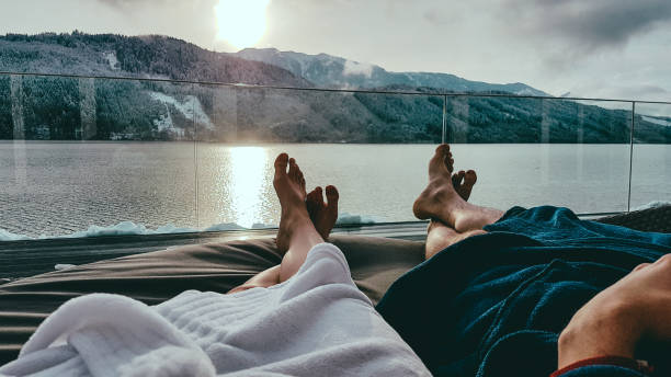 Austria-bathhouse Millstätter Lake Couple relaxing on the sun beds in Spa, Badehaus Millstätter See, Austria, by Millstätter See. Only the legs are visible and some parts of bathrobes. Snowy mountains in the back, snow on the terrace travel hotel accommodations stock pictures, royalty-free photos & images