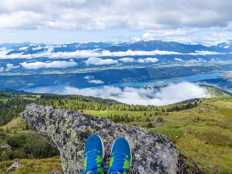 Blue shoes resting on the rock in Millstatt, Granattor, Austria. Clouds in the valley. Dense forest around. Milstätter Lake in the bottom.  Some cows on the meadow.