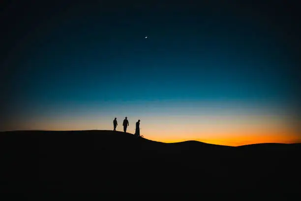 Photo of Arabs on the sand dunes walking behind each other during twilight