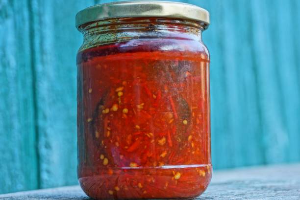 un bocal en verre avec du poivre rouge en conserve et de la sauce se dresse sur la table contre le mur vert - chutney jar tomato preserved photos et images de collection