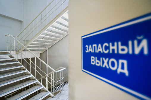 Moscow, Russia - 5 April, 2018: Emergency exit sign out of focus in Russian and multi-flight stairway in modern house.