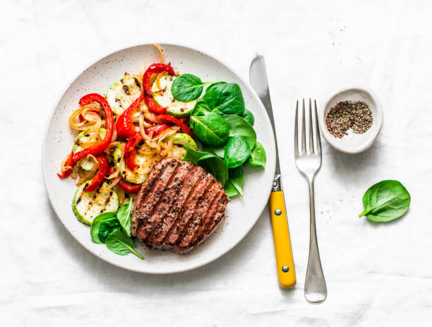 istock Beef steak with grilled  vegetables, sweet pepper, zucchini and fresh spinach on a light background, top view. Delicious healthy balanced lunch 1130980909