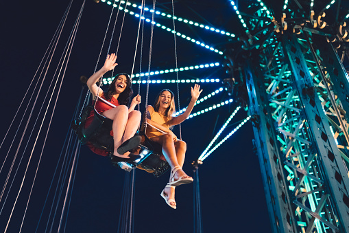 Girls on swing ride at night waving to friends from above