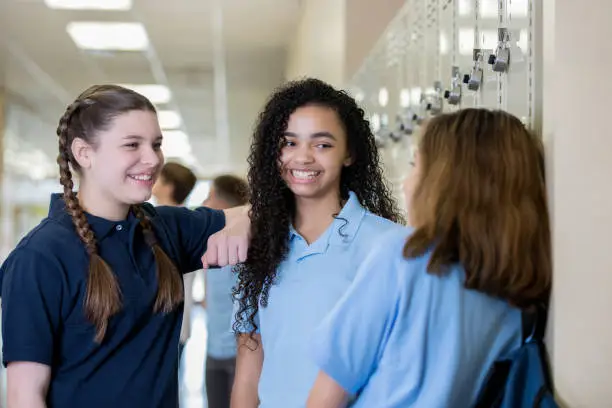 Photo of Diverse group of teenage high school girls talking in private school hallway near lockers
