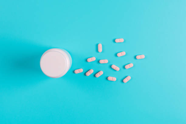 istock Pink pills, tablets and white bottle on blue background.  Copy space for text 1130982680