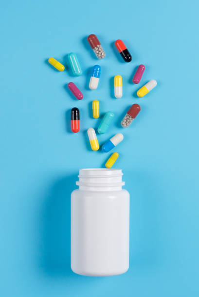 istock Colored pills, tablets and white bottle on blue background.  Copy space for text 1130982700