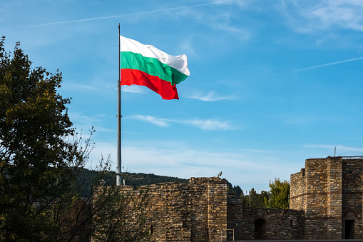 Bulgarian flag well illuminated with late afternoon sunshine flys from flagpole over ancient stone walls of Tsarevets Fortress, Veliko Tarnovo, Bulgaria
