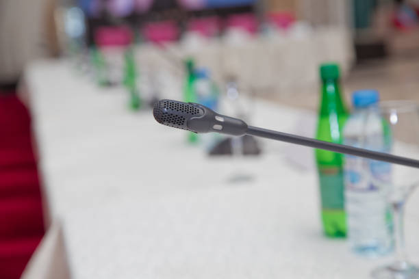 istock Microphone in the empty conference - meeting room . Intercom in the classroom. Table microphone on the wooden table in the meeting room. Blur background and selective focus. 1130986470