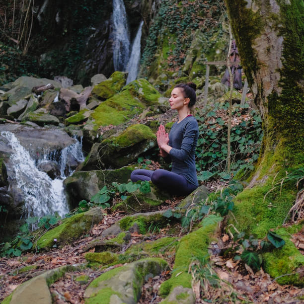 istock Young slim woman practicing yoga outdoors in moss forest on background of waterfall. Unity with nature concept. Girl meditates sitting 1130986772
