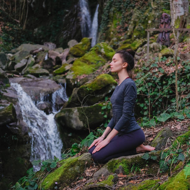 istock Young slim woman practicing yoga outdoors in moss forest on background of waterfall. Unity with nature concept. Girl meditates sitting 1130986775