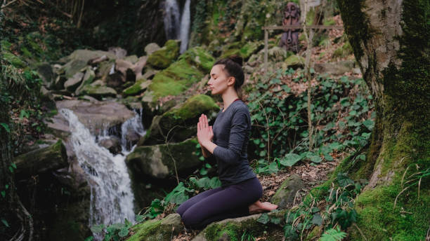istock Young slim woman practicing yoga outdoors in moss forest on background of waterfall. Unity with nature concept. Girl meditates sitting 1130986778