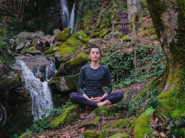 istock Young slim woman practicing yoga outdoors in moss forest on background of waterfall. Unity with nature concept. Girl meditates sitting 1130986782