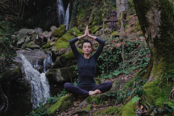 istock Young slim woman practicing yoga outdoors in moss forest on background of waterfall. Unity with nature concept. Girl meditates sitting 1130986784