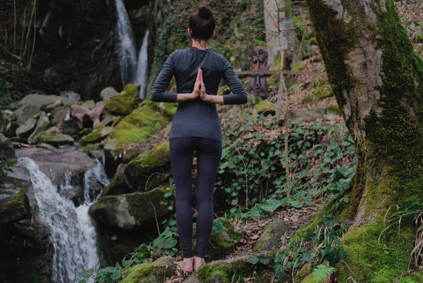 istock Young slim woman practicing yoga outdoors in moss forest on background of waterfall. Unity with nature concept. Girl standing with prayer hands 1130986787