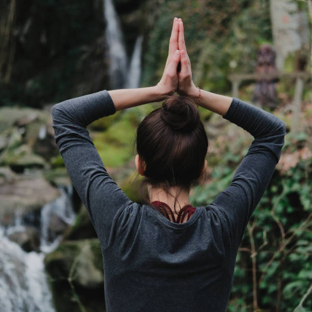 istock Young slim woman practicing yoga outdoors in moss forest on background of waterfall. Unity with nature concept. Girl standing with prayer hands 1130986790