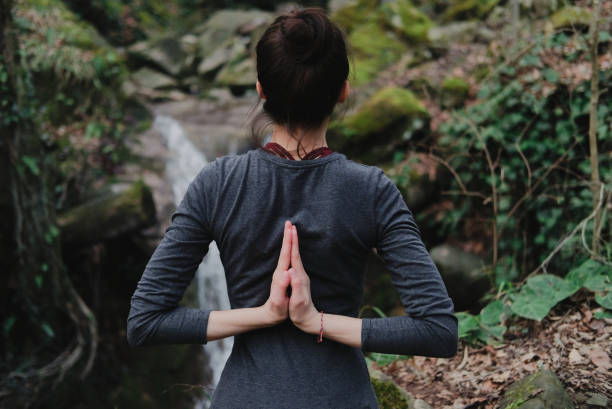 istock Young slim woman practicing yoga outdoors in moss forest on background of waterfall. Unity with nature concept. Girl standing with reverse prayer hands back 1130986792