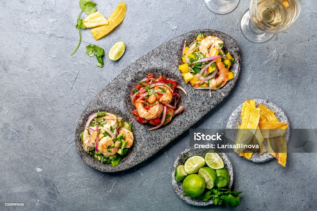 CEVICHE. Three colorful shrimps ceviche with mango, avocado and tomatoes. Latin American Mexican Peruvian Ecuadorian food. Served with white wine and banana chips Coloresd ceviches with mango, avocado and tomatoes. White wine, lime and banana chips Peru Stock Photo