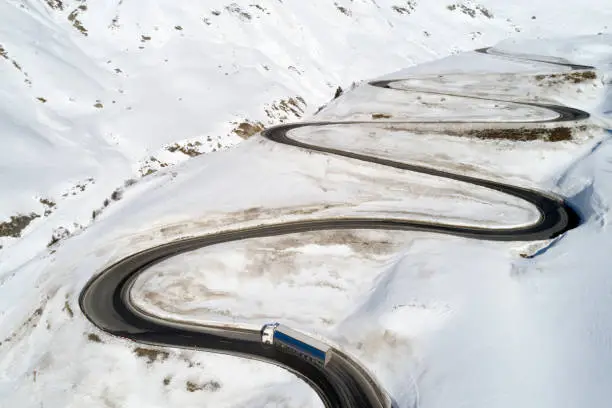 Aerial view of semi truck driving on curvy, winding Alpine road in winter, Julier Pass, Canton of Graubunden, Switzerland.
