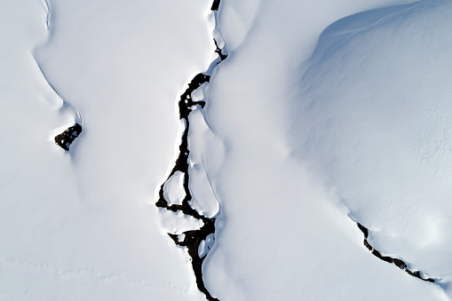 Aerial view of abstract natural pattern, winter landscape with a mountain stream in Swiss Alps.